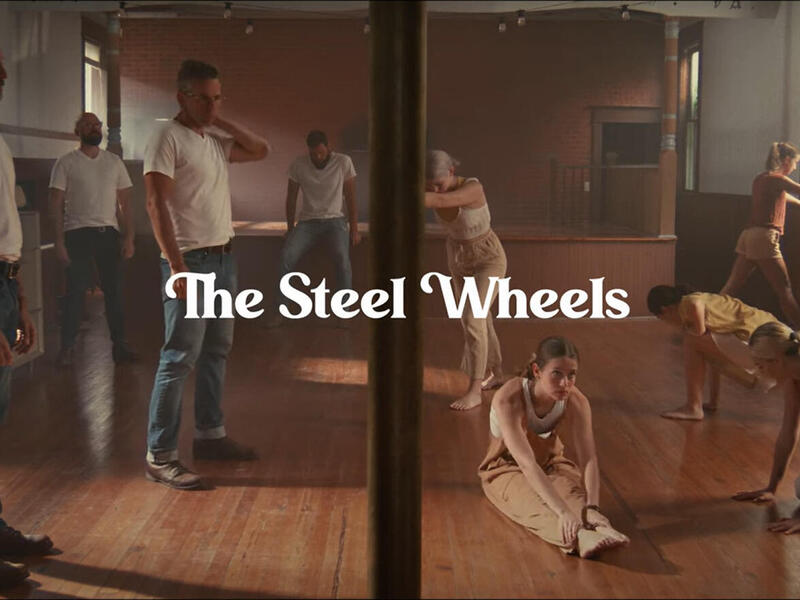 A photo of five men standing on the left side of a room and five young women stretching on the other side of it. 