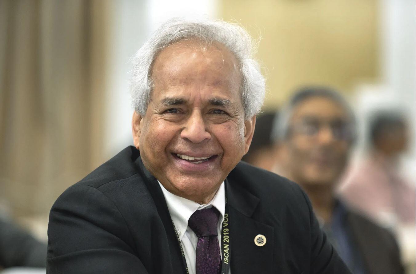 A man smiling while wearing a black sport coat and tie over a white button down shirt. 