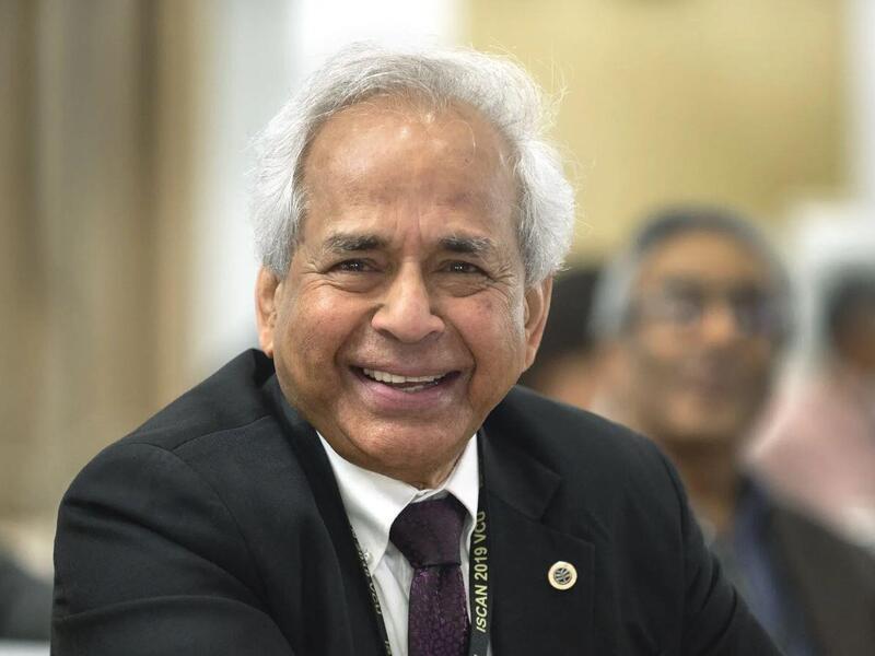 A man smiling while wearing a black sport coat and tie over a white button down shirt. 