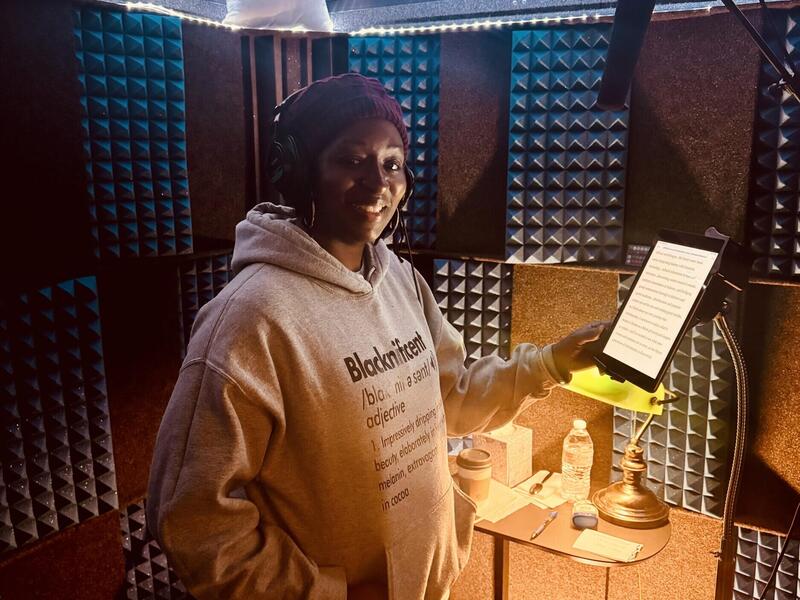 A woman in a hooded sweatshirt stands in front of a microphone.