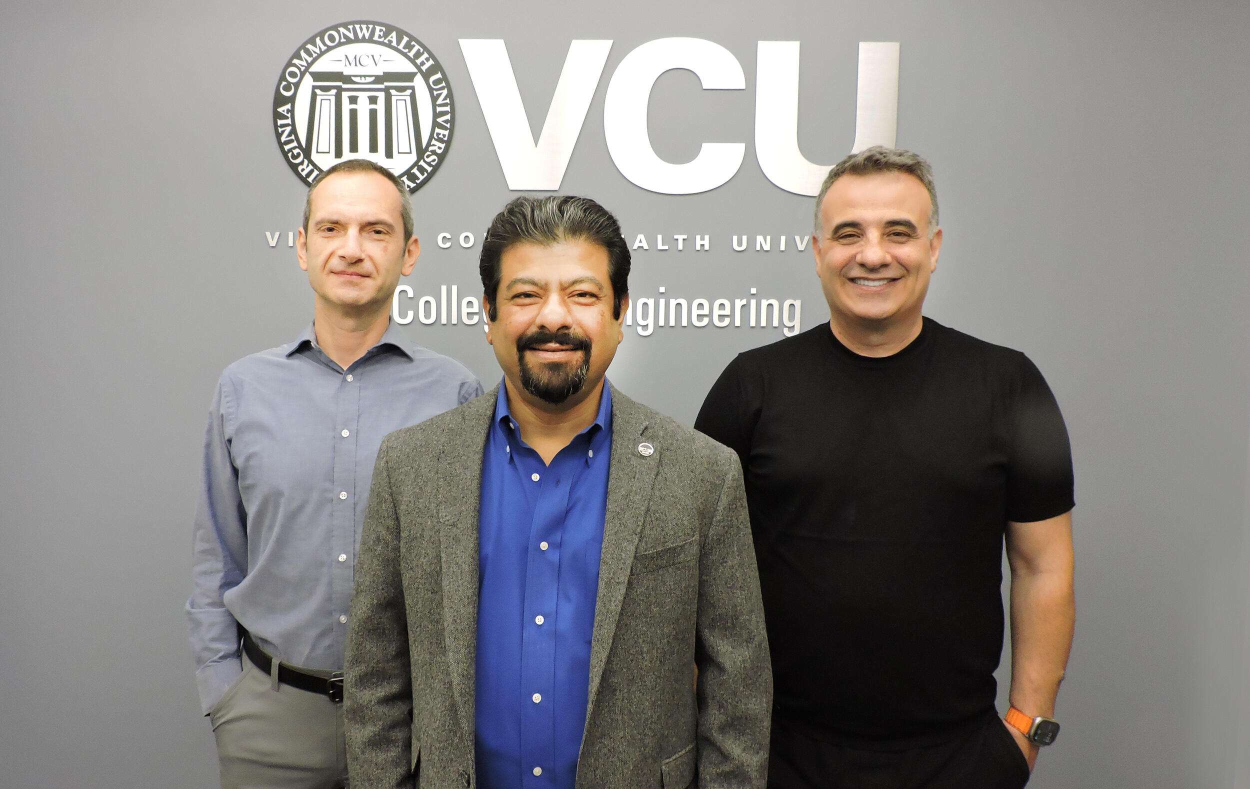 Three men stand in front of a College of Engineering sign.