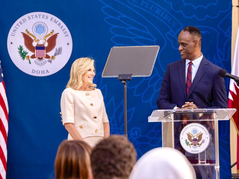 A photo of a man standing at a podium looking at a woman standing to his left. 