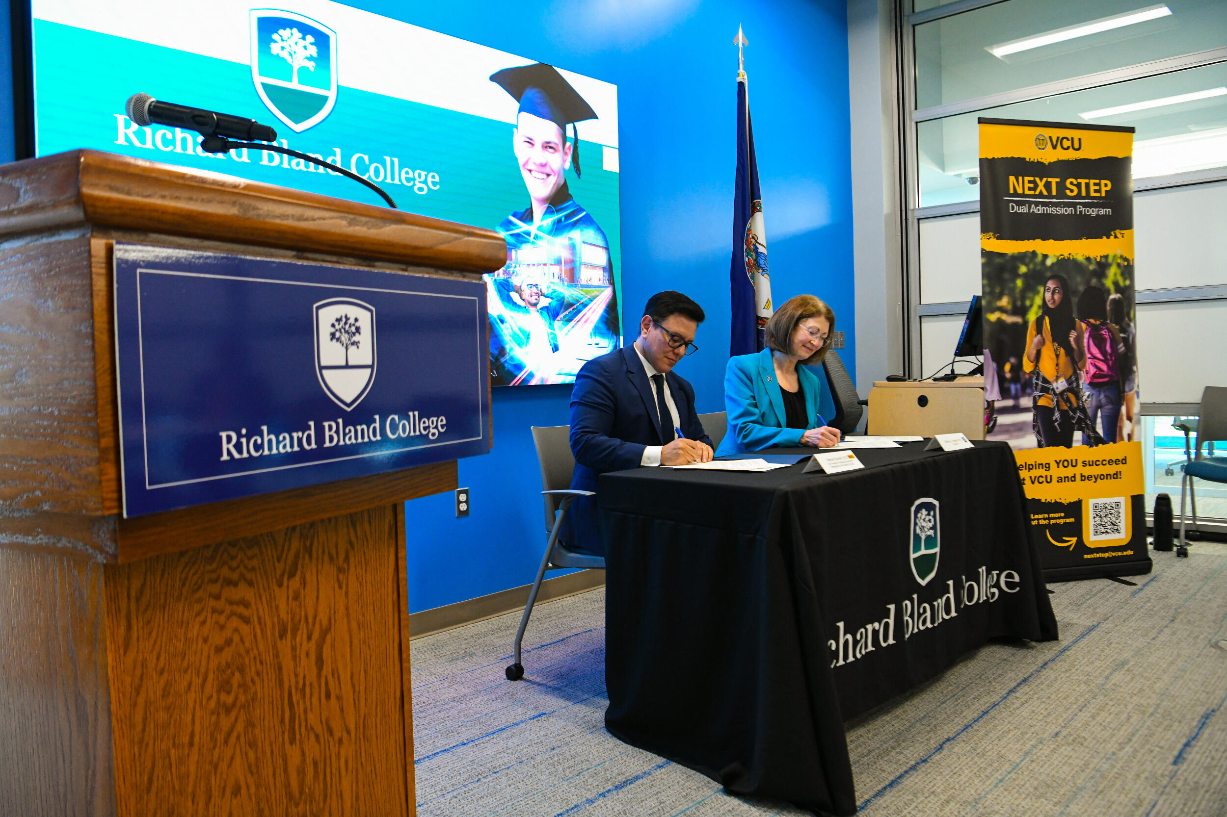 A man and a woman sit at a table and sign documents next to each other.
