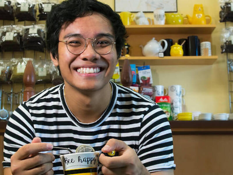 Jon Mirador holding a teacup and steeper. A wall full of tea accessories sits behind him.