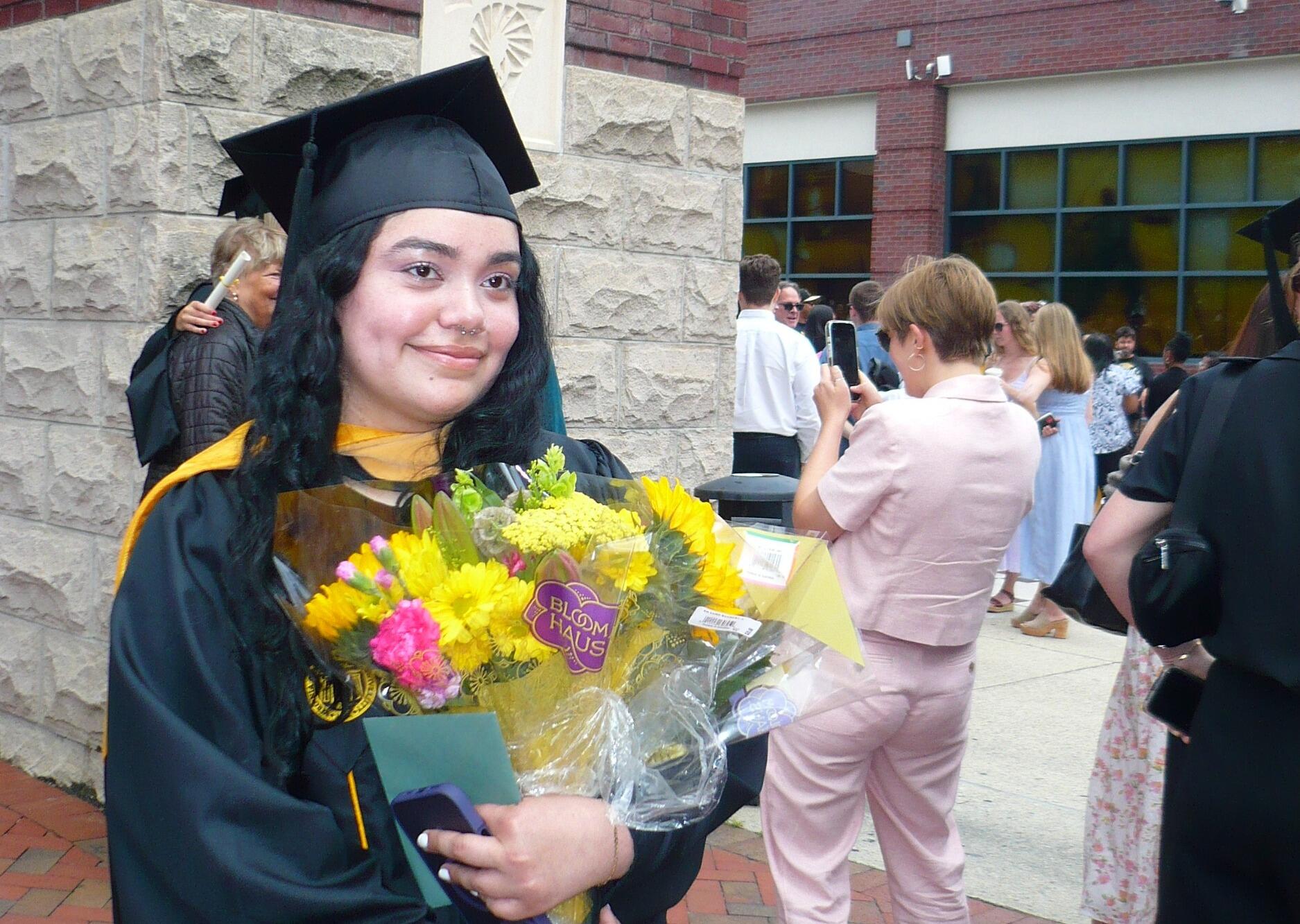 A photo of a woman wearing a graduation cap and gown holding a bouquet of flowers. 