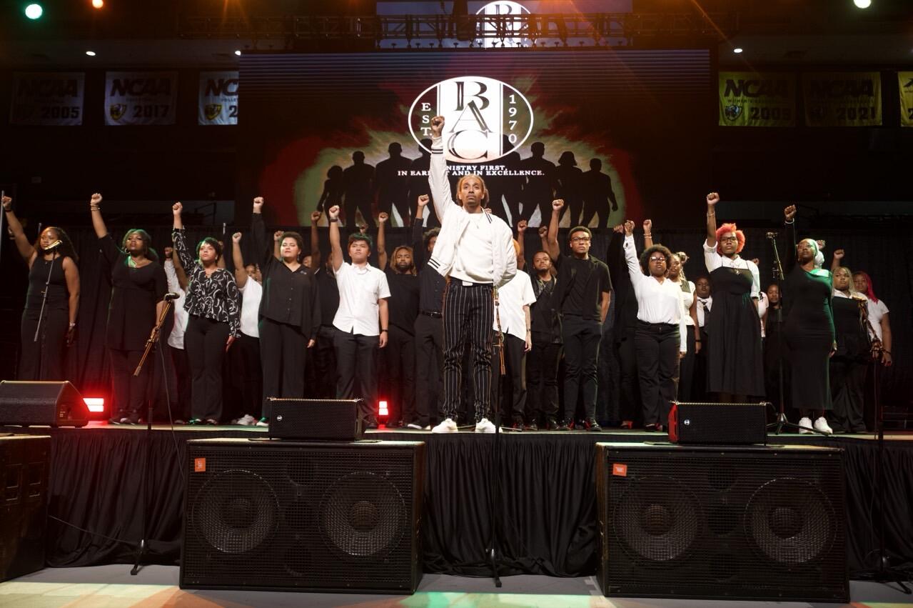 The Black Awakening Choir performs on stage, all raising their fists in uniform.