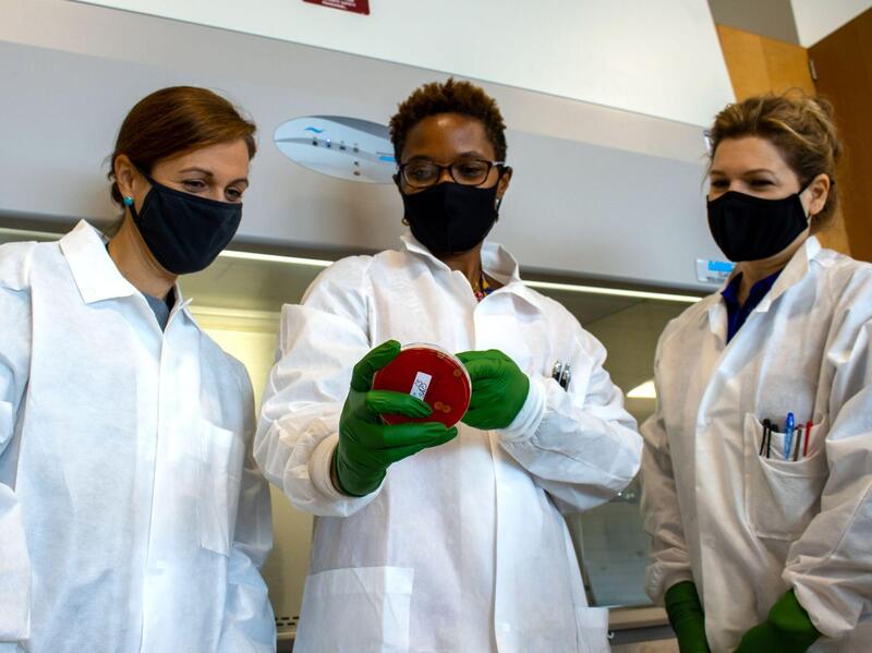 Three women in lab coats examine a sample.