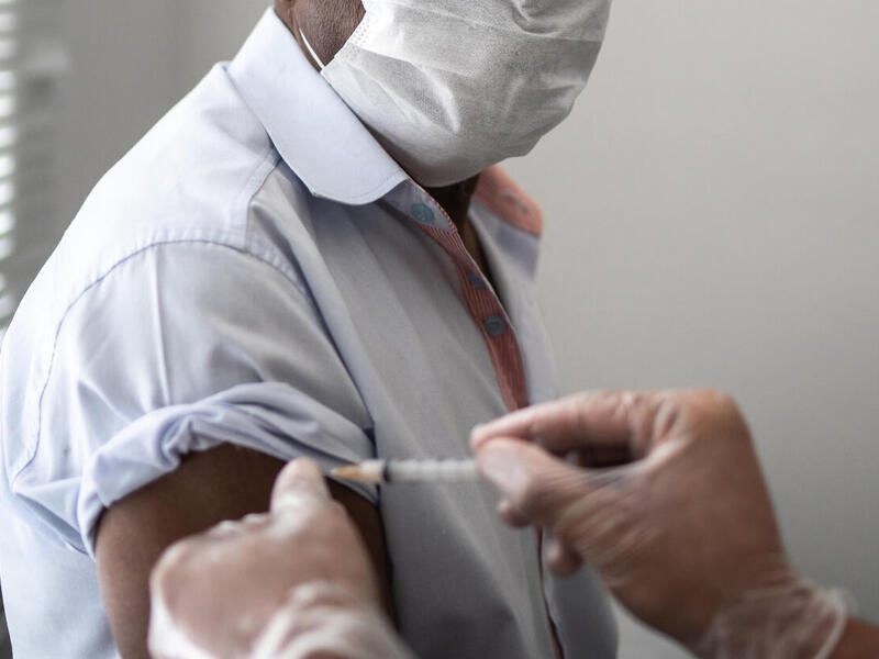 A person wearing a mask receives a vaccination shot.
