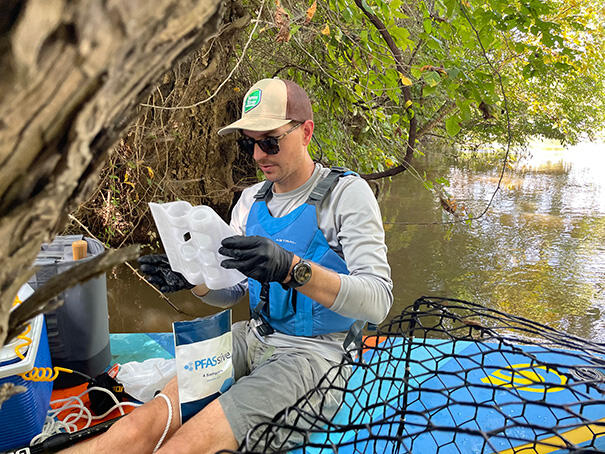 A photo of a man reading a sheet of paper next to a river. 