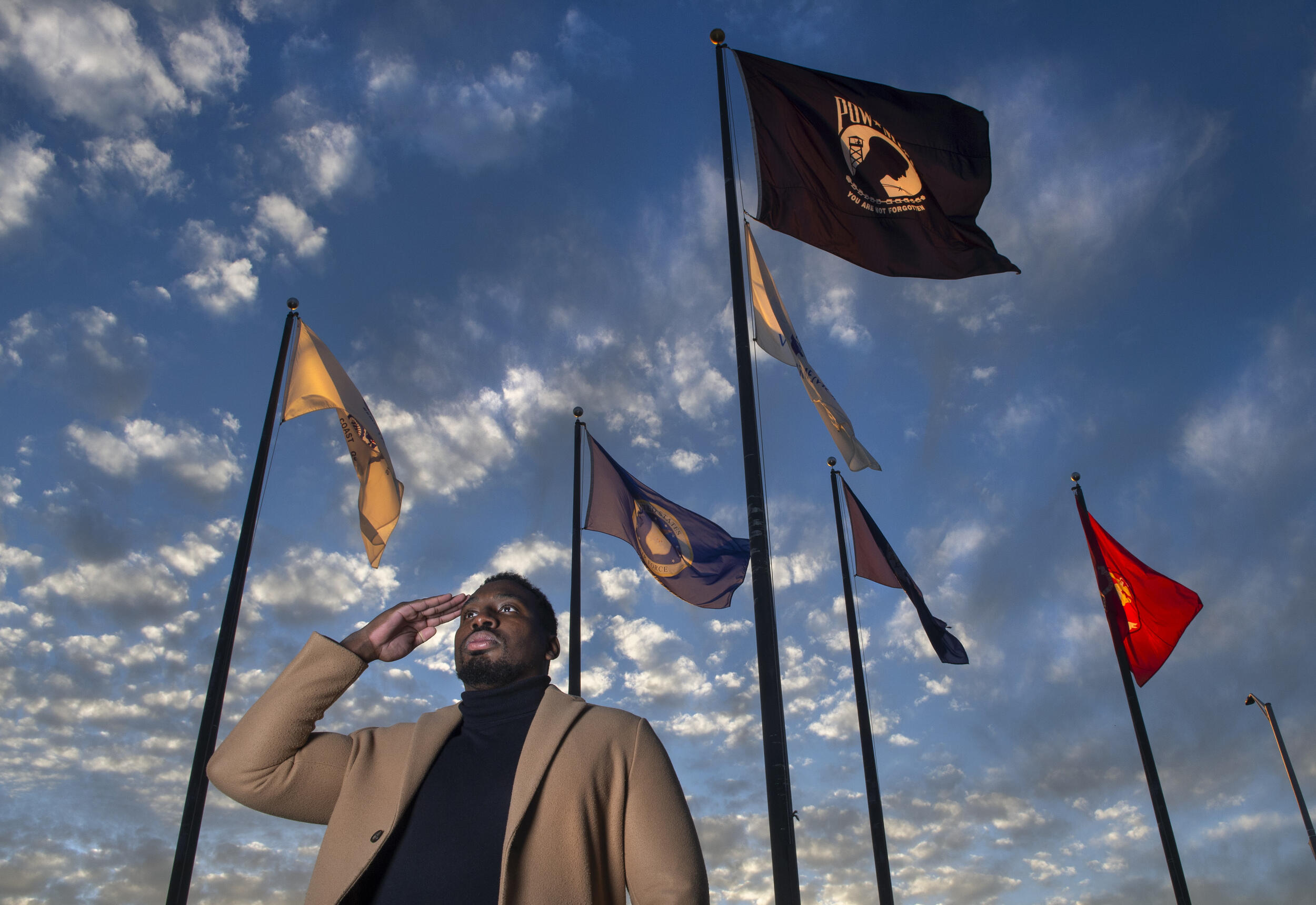 A photo of a man saluting in front of six flags. 