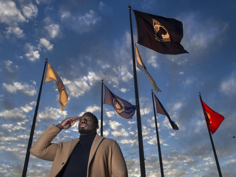 A photo of a man saluting in front of six flags. 