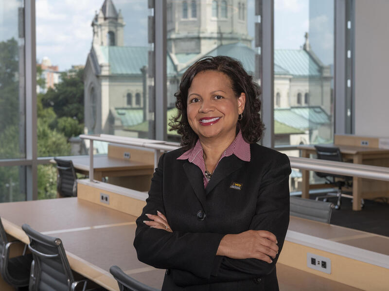 A photo of a woman standing. She has her arms crossed against her chest and is smiling. 