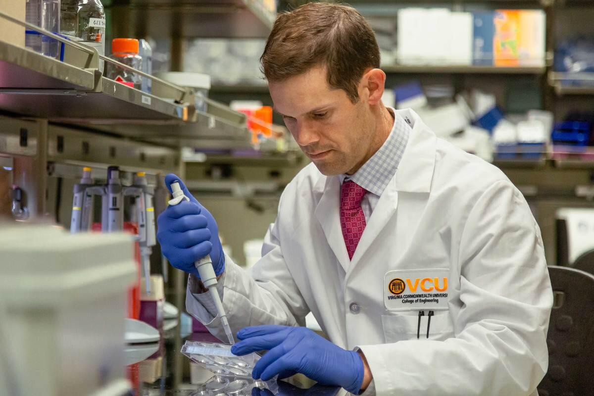 Michael McClure wearing a lab coat and gloves holding equipment at a work station 