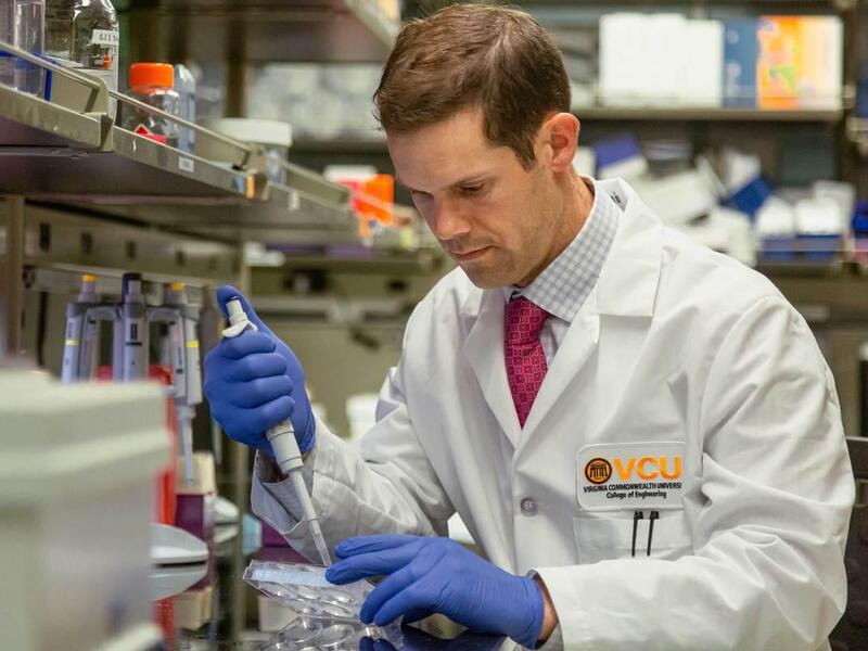 Michael McClure wearing a lab coat and gloves holding equipment at a work station 
