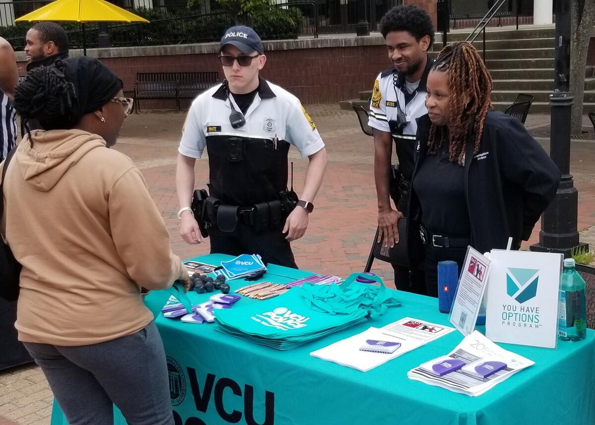 A photo of three police officers standing behind a booth, talking to a woman on the other side of the booth. 