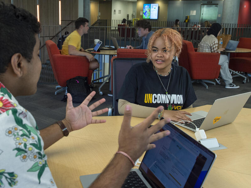 A photo of two people sitting at a table with laptops. 