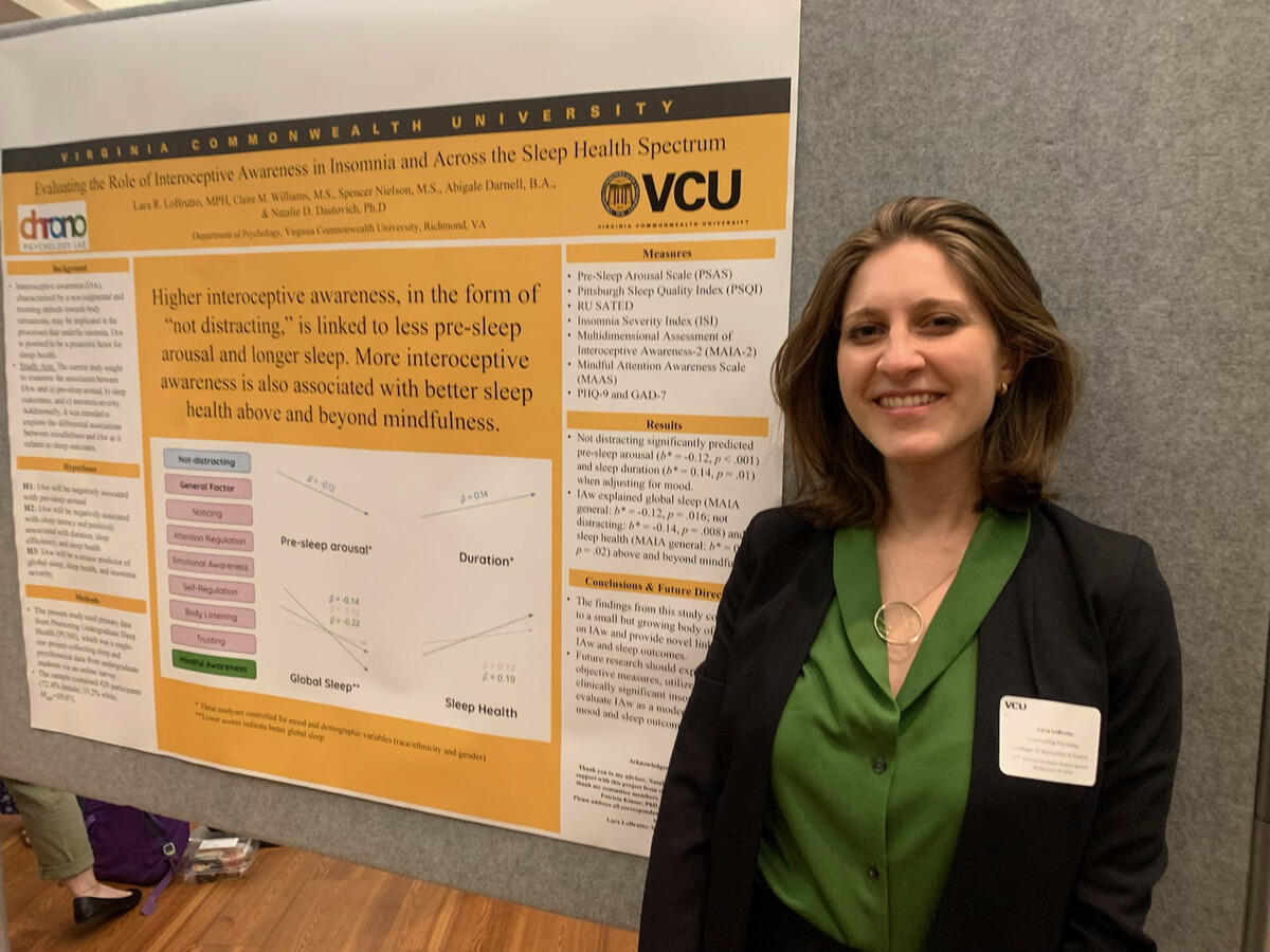 A photo of a woman from the chest up standing to the right of a poster. 