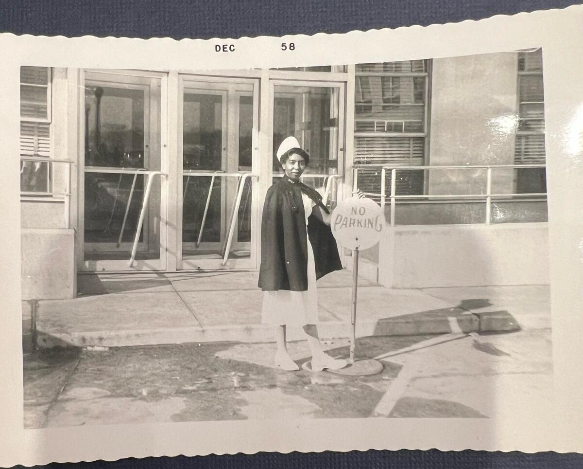 A black and white photo of a woman wearing a nurse uniform in front of a building 