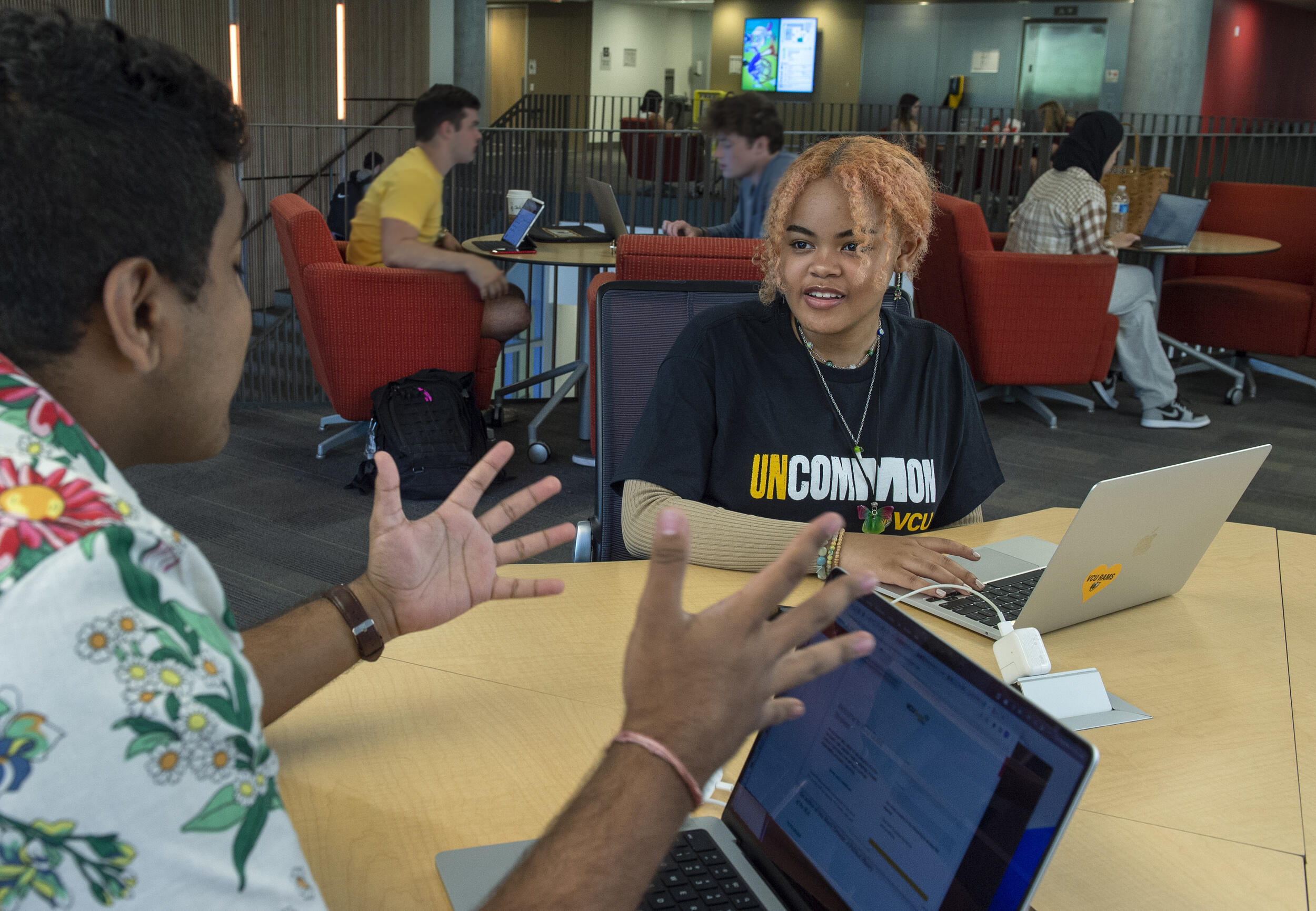 Two students sitting at a table with laptops in front of them. 
