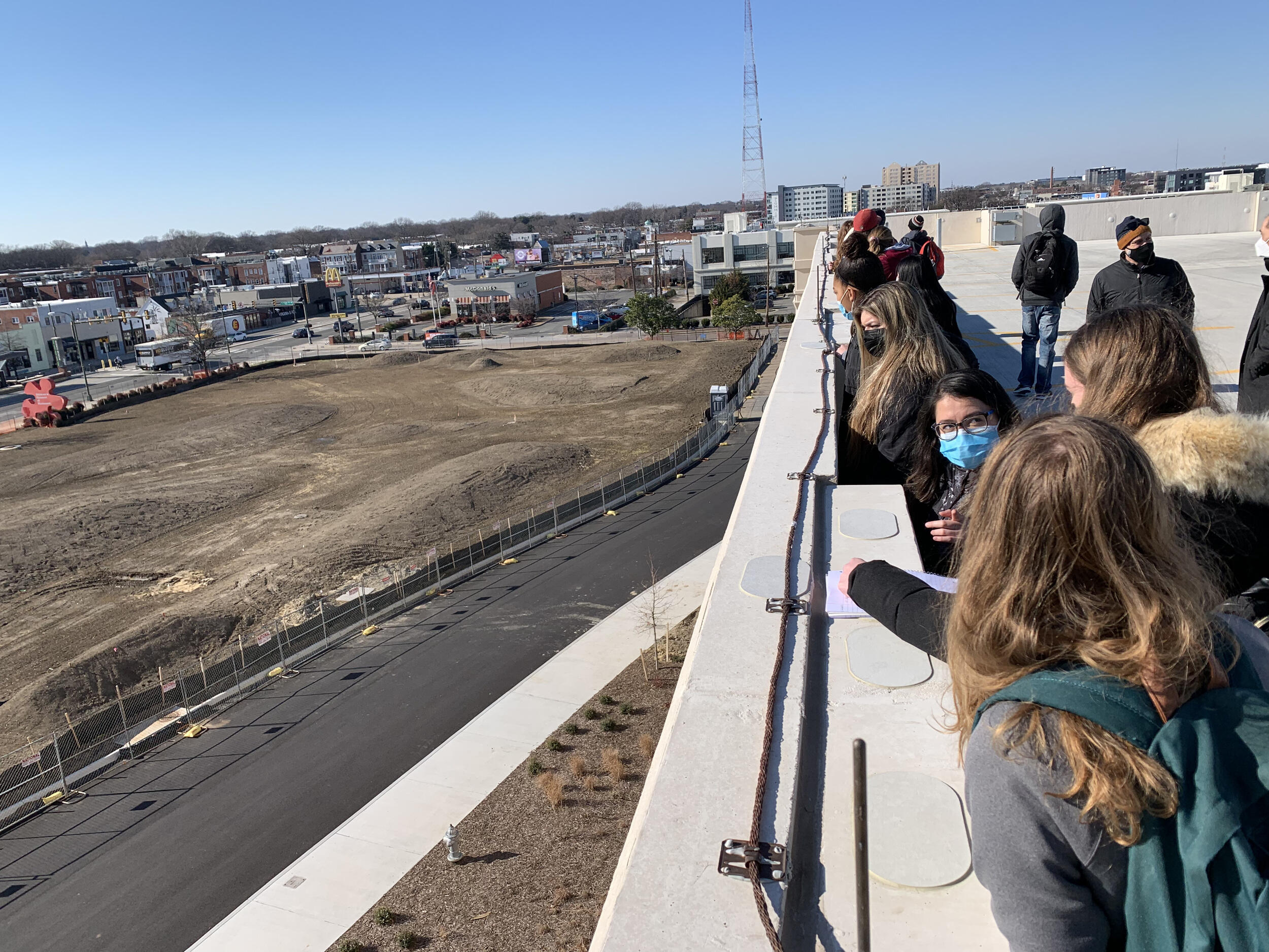A group of students on the right looking at an patch of land on the left that is mostly just dirt 