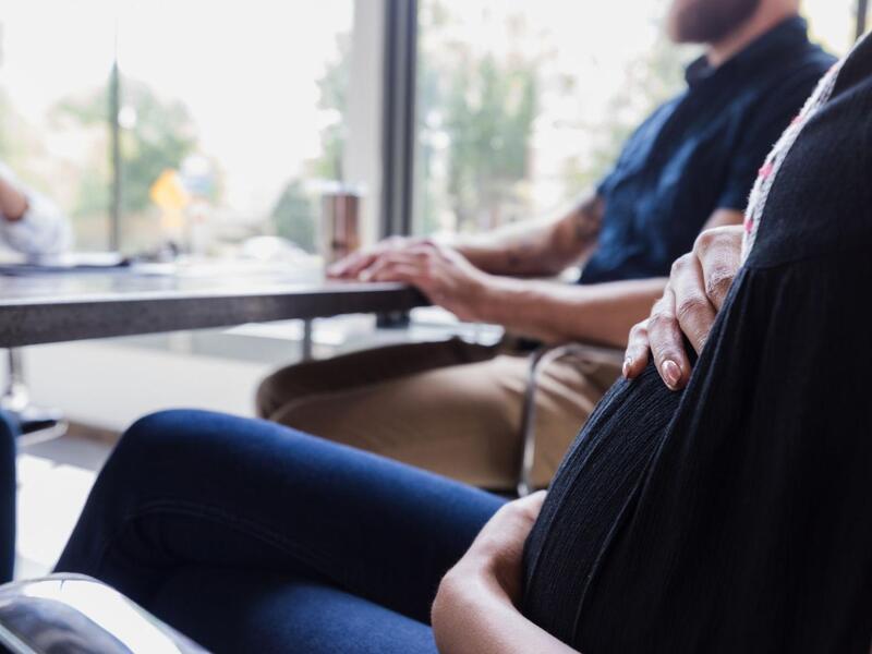 A stock image of two people sitting on one side of a desk and a woman sitting on the the other side of it talking to them. 