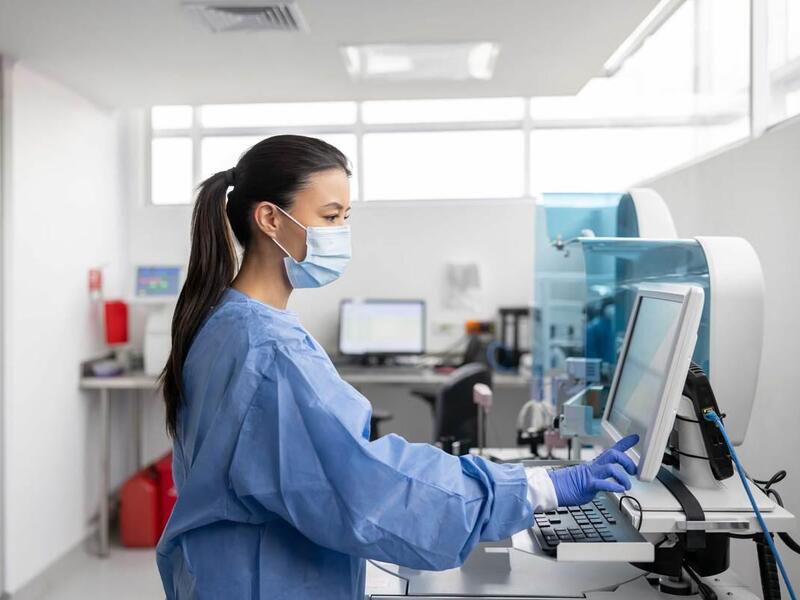 A person in medical gear standing while looking at a computer screen