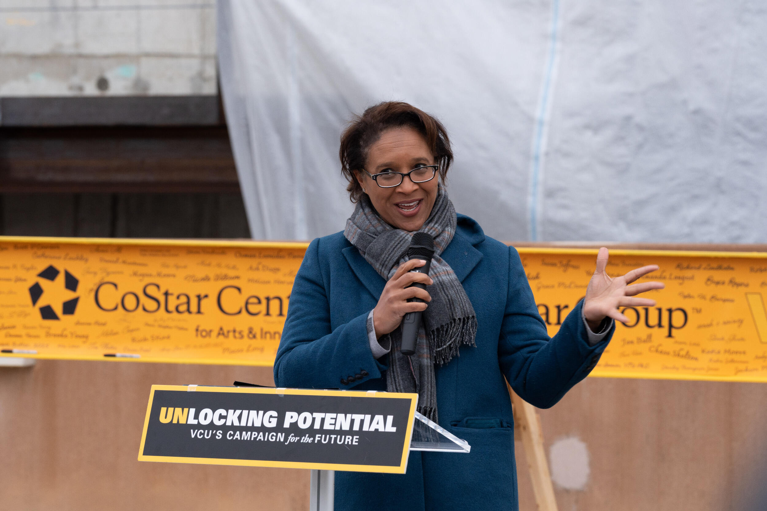 A photo of a woman standing behind a lectern and speaking into a microphone. 