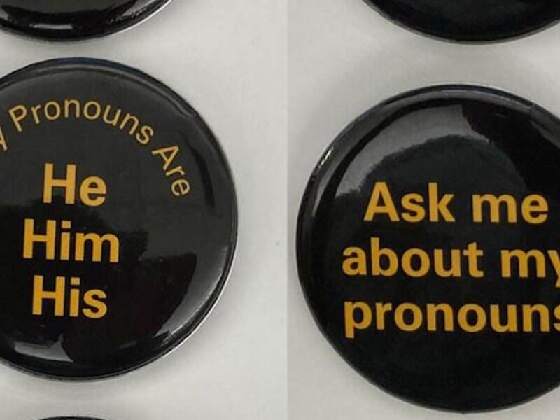 Two black buttons with yellow text. The first says \"My Pronouns Are He Him His\" and the second says \"Ask me about my pronouns\" 