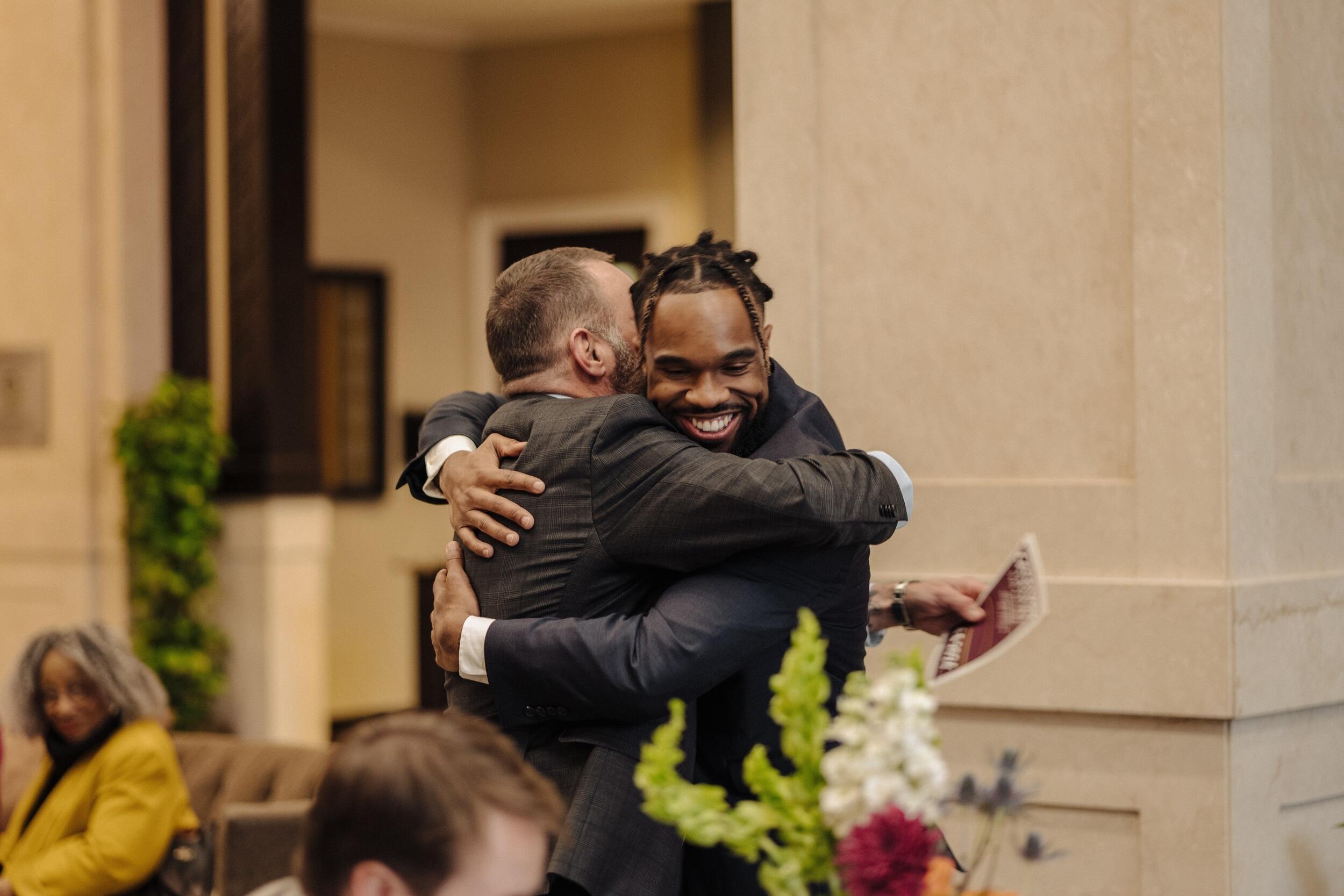 A photo of two men hugging. The man who's face is visable is smiling. 