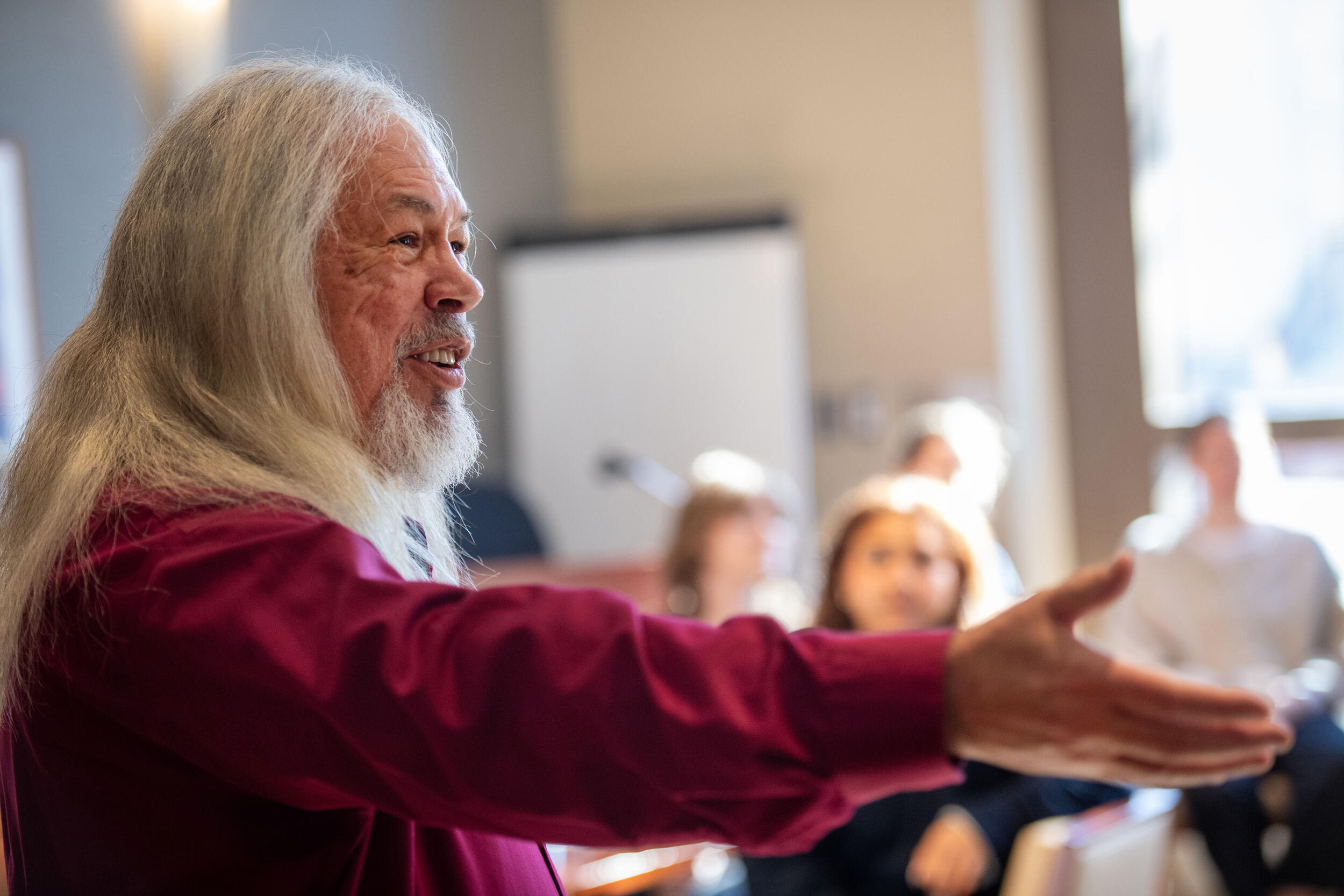 A photo of a man from the chest up. He is speaking to a crowd and extending his right arm to the side. 