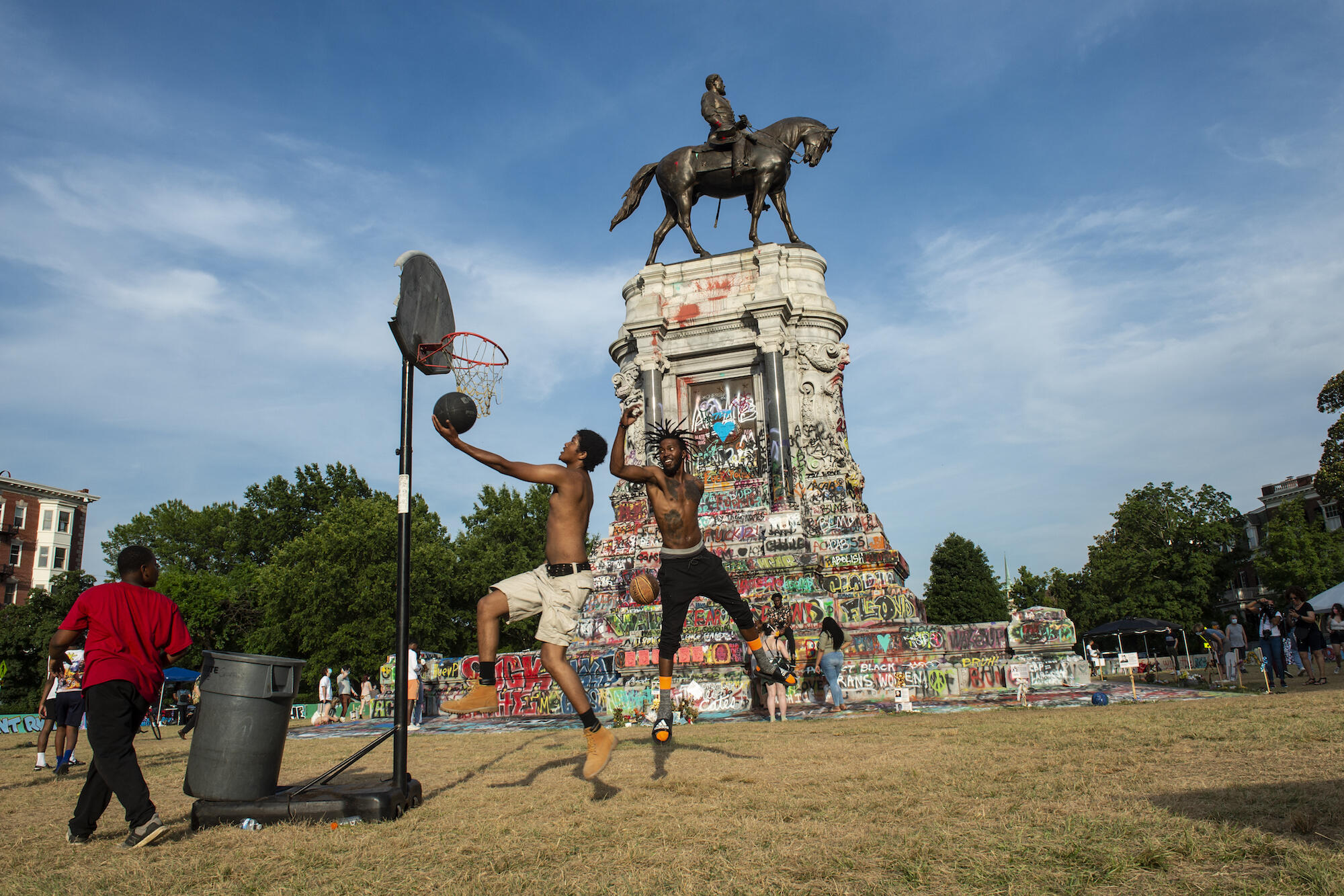 Young men playing basketball inside Marcus-David Peters Circle, with the graffiti-covered Robert E. Lee Memorial in the background.
