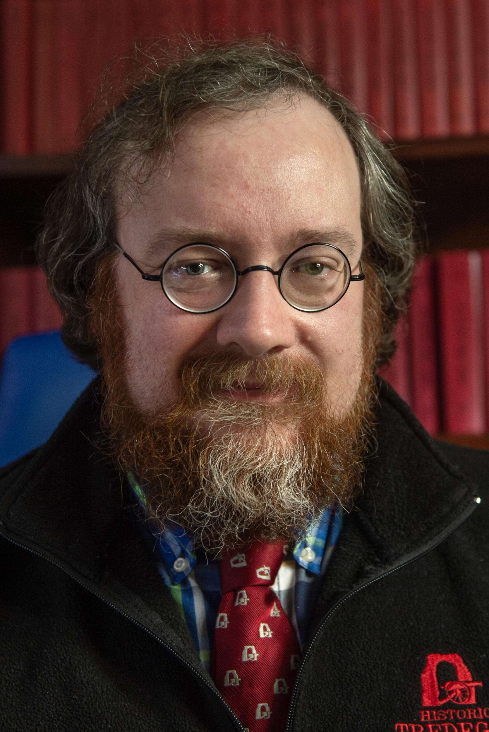 A photo of a man from the shoulders up. He is wearing circular glasses and has a beard. 