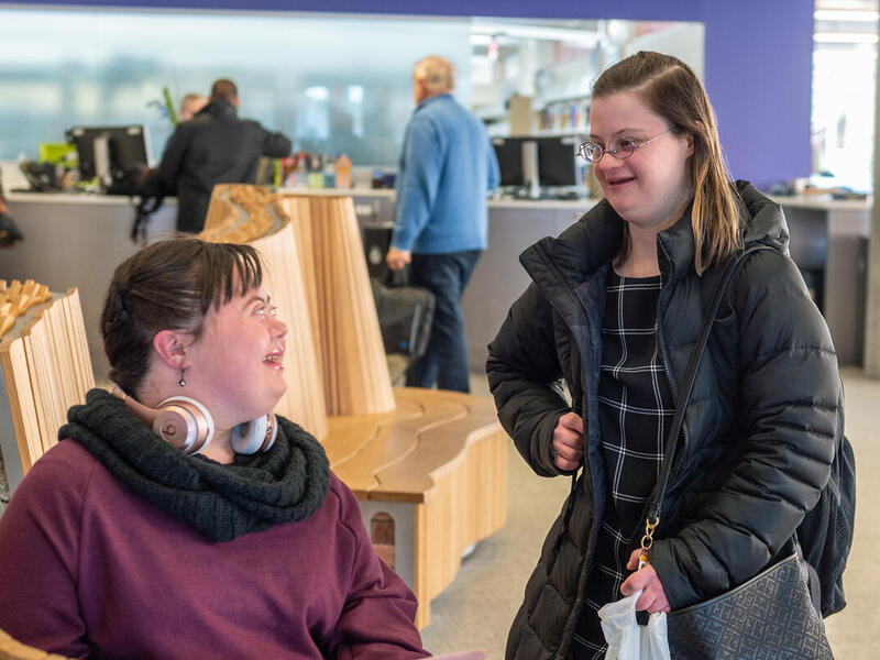 A photo of a woman sitting smiling at a woman who is standing next to her on the right. 
