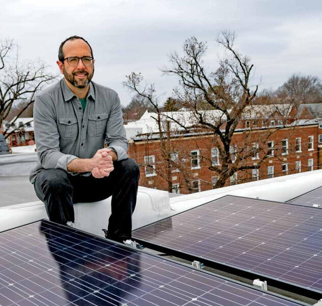 A man sitting on a roof behind of solar panels. 