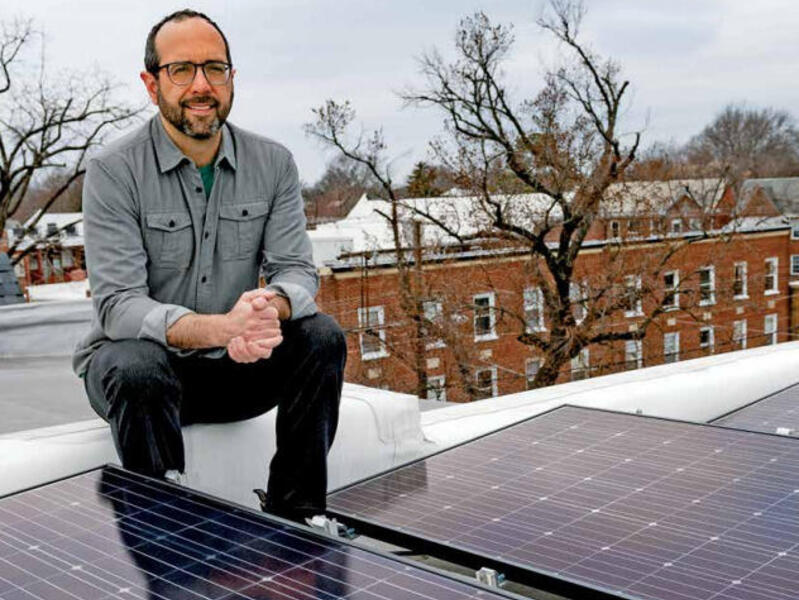 A man sitting on a roof behind of solar panels. 