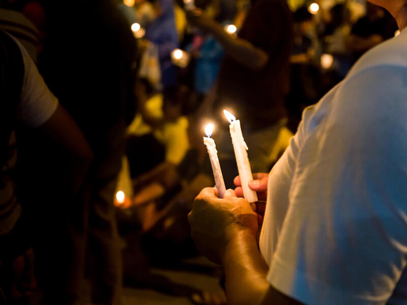 A photo of a person holding two candles in their hands in a crowd of people holding candles. 