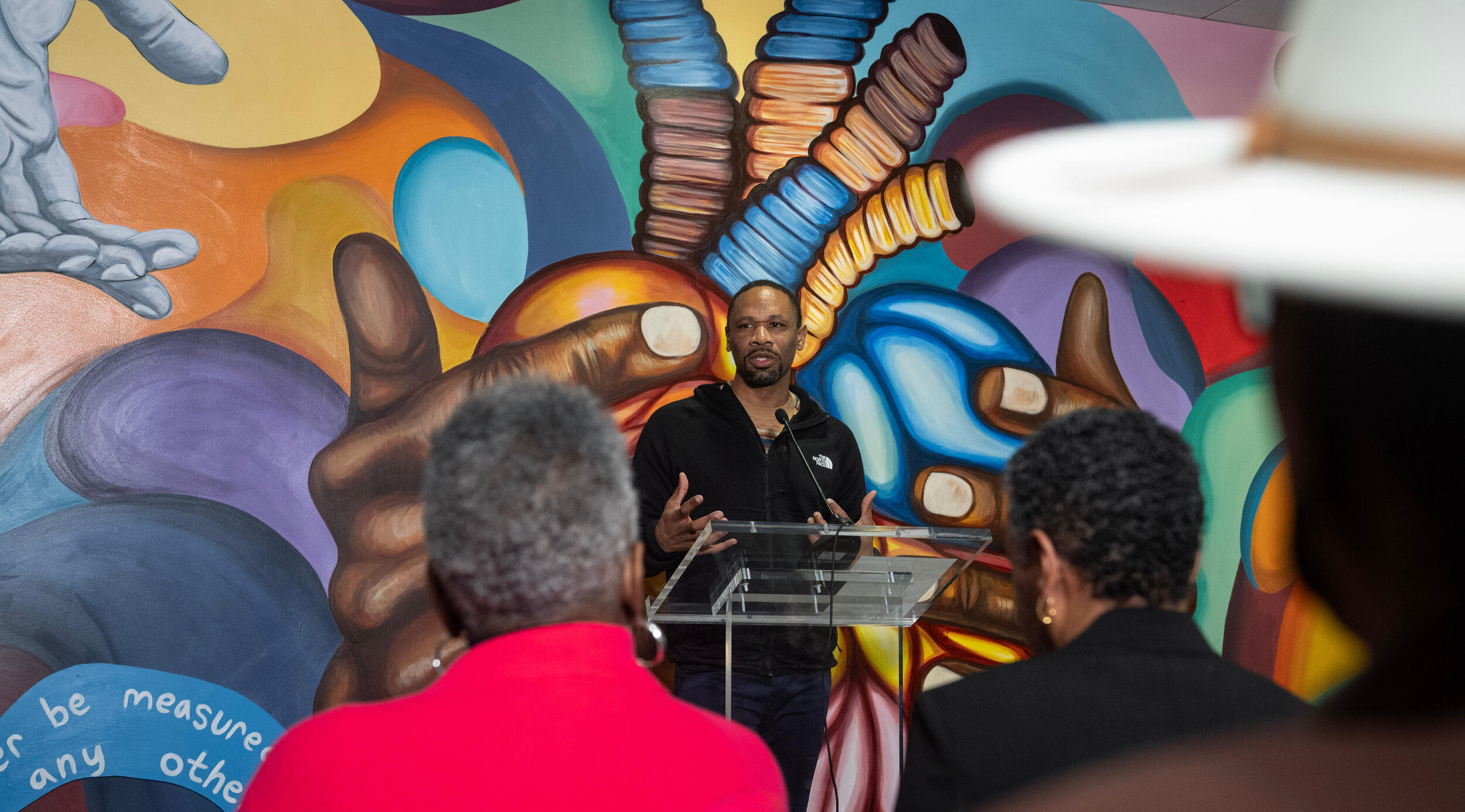 A man speaks at a lectern in front of a mural.
