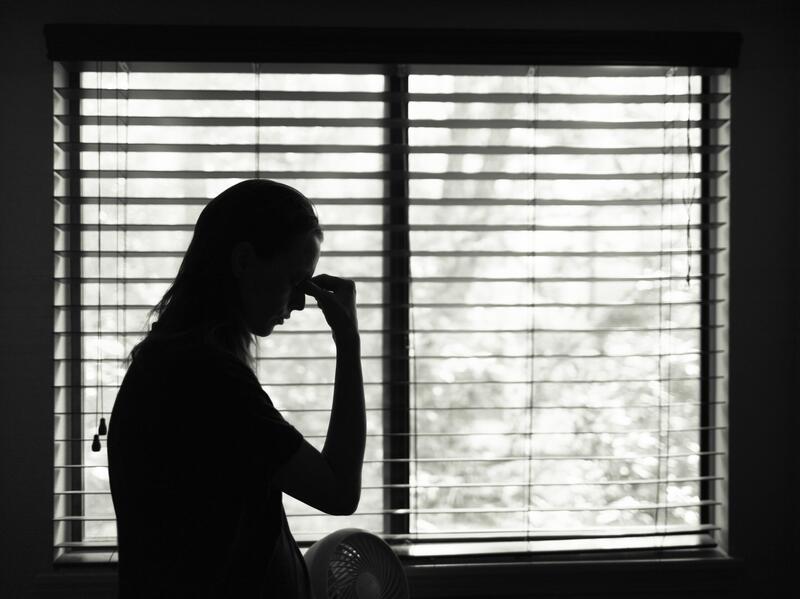 The silhouette woman pinching the brow of her nose in front of a window