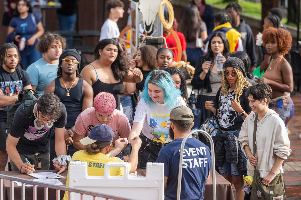A photo of a few lines of people standing behind a table with sign up sheets. Behind the table are two people wearing \"staff\" t-shirts