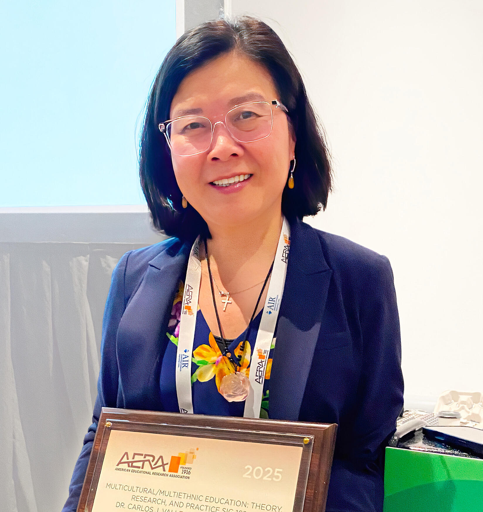 A woman in glasses smiles and holds a framed award.