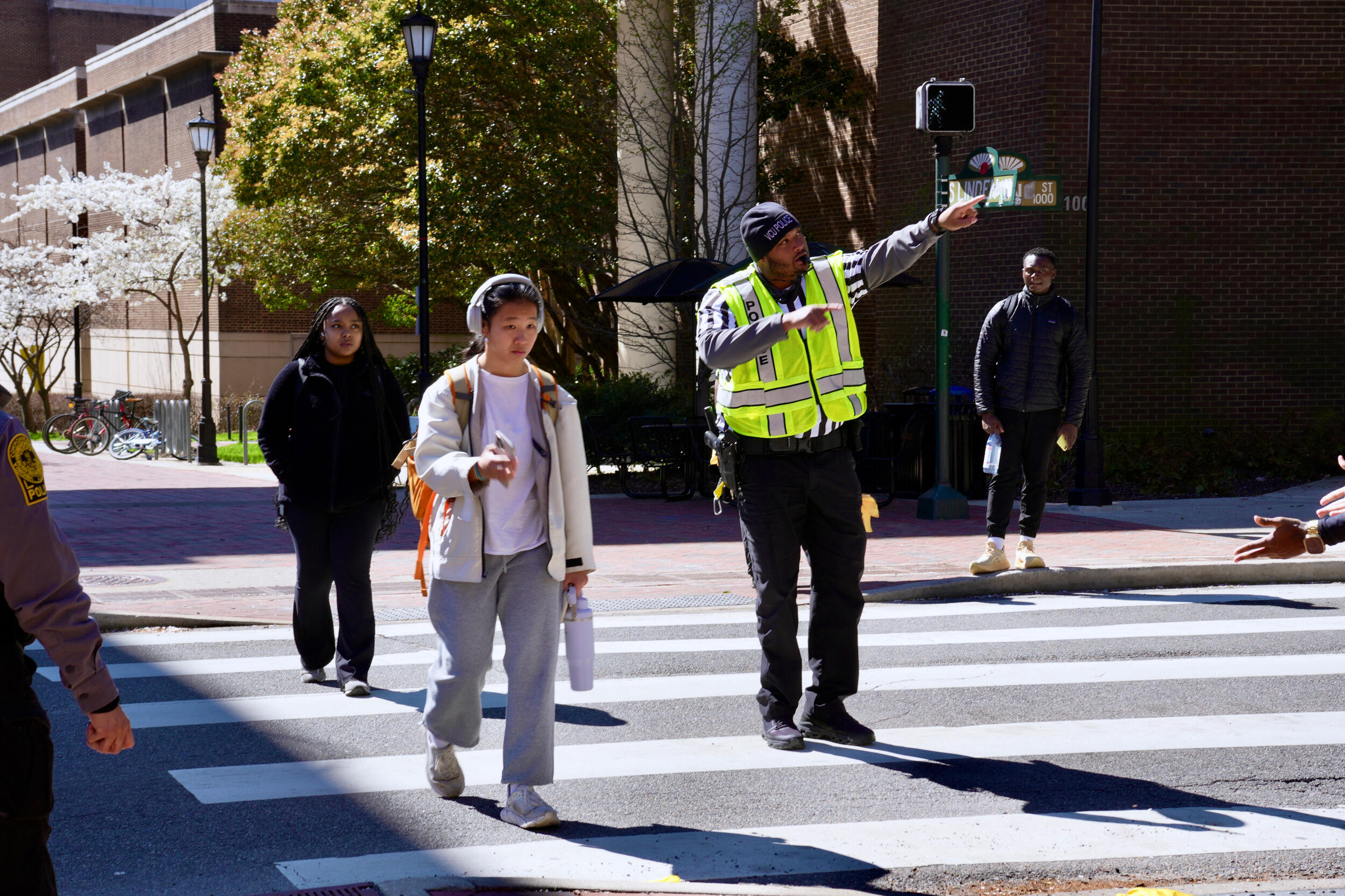 A police officer in a crosswalk gestures while others cross the street in the crosswalk.