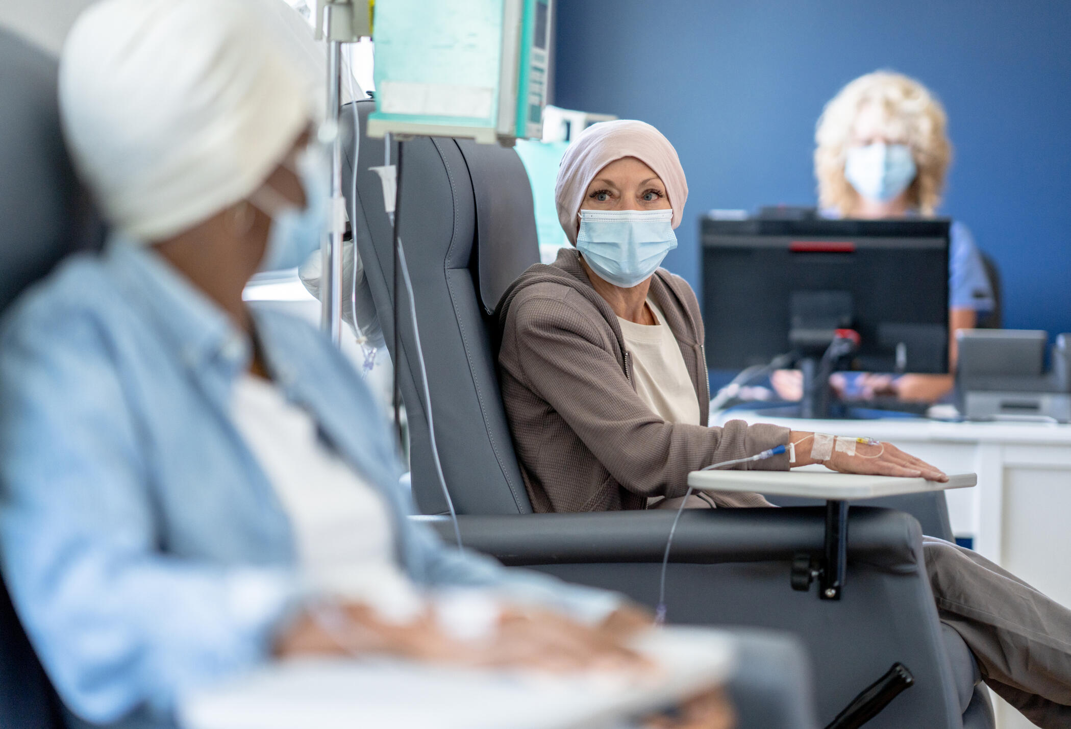 Two patients sitting in chairs wearing face masks with IVs in their arms. 