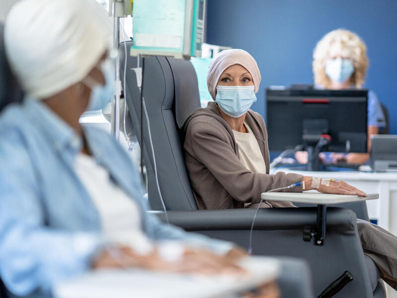 Two patients sitting in chairs wearing face masks with IVs in their arms. 
