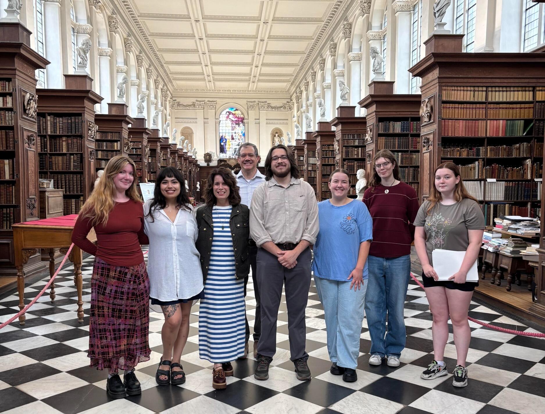 A group photo of eight people standing in a library. 