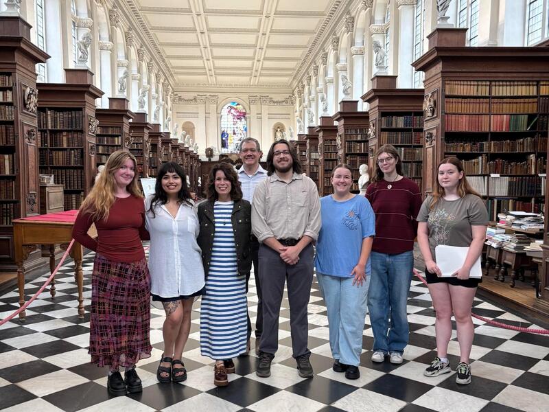 A group photo of eight people standing in a library. 