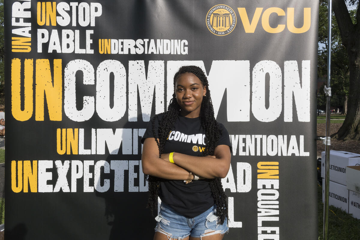 A woman standing with her arms crossed in front of a poster that says \"Uncommon\" 