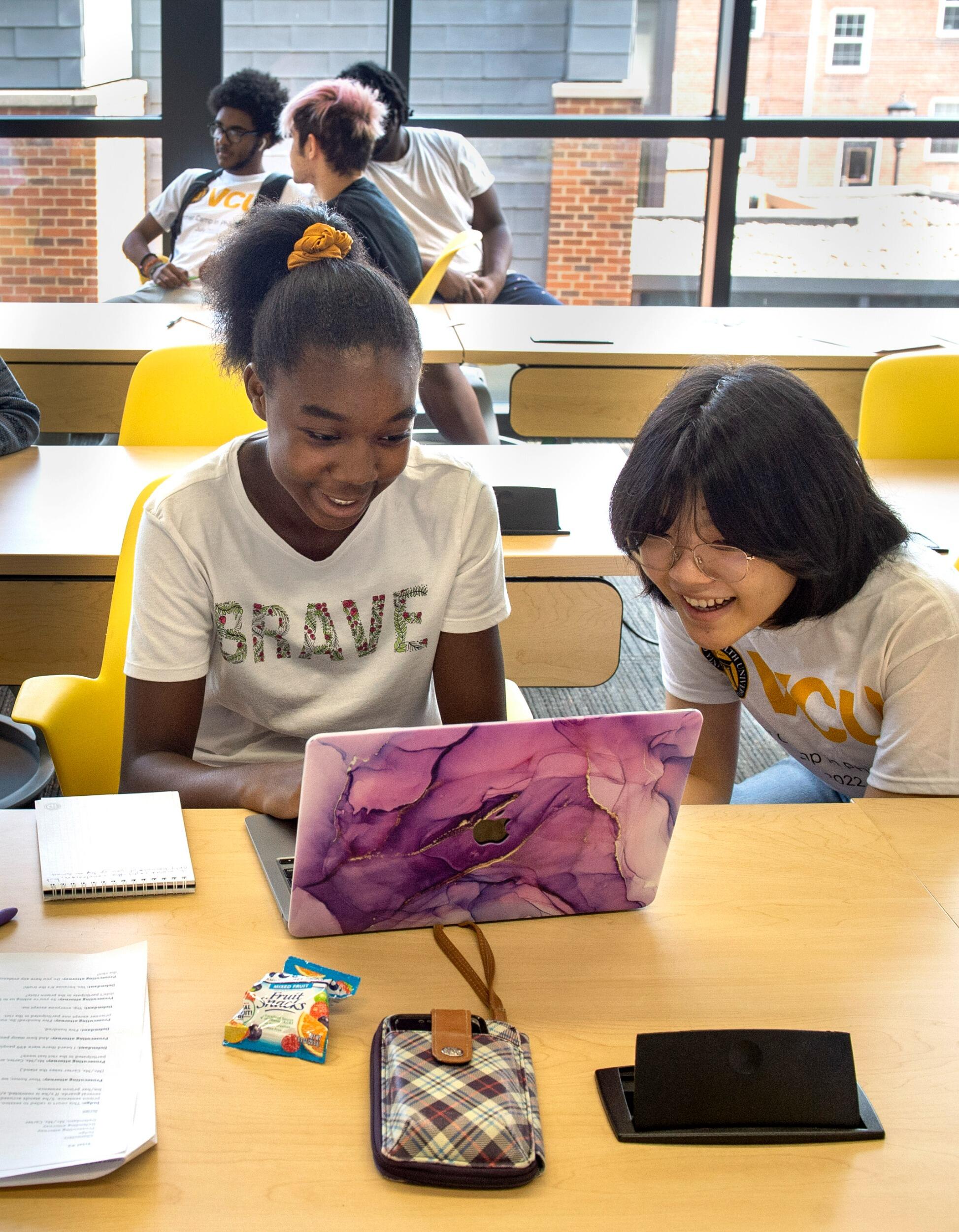 Rita, left, and Eve, local high school students, smile as they look at the screen of a laptop.