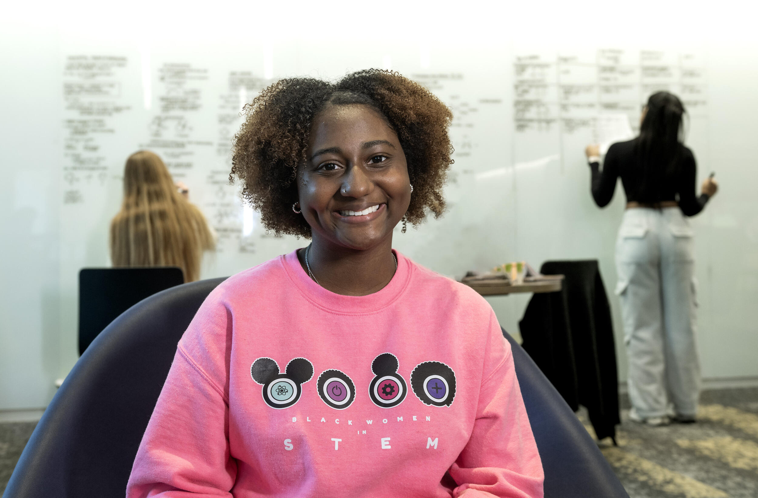 A photo of a woman in a pink sweatshirt sitting in a chiar. 