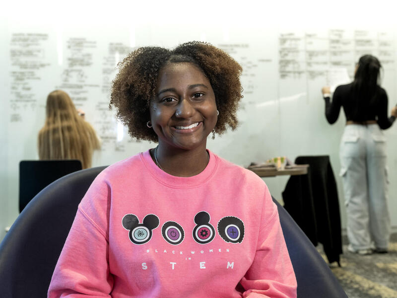 A photo of a woman in a pink sweatshirt sitting in a chiar. 