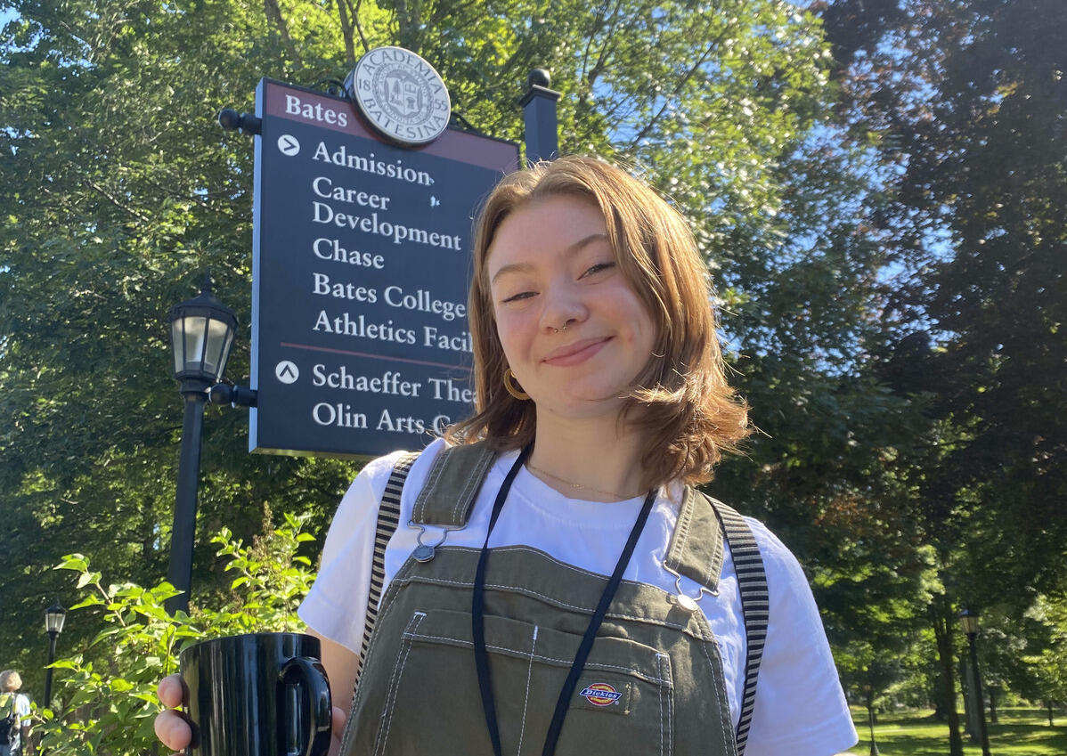 A woman wearing overalls standing outside in a park. 